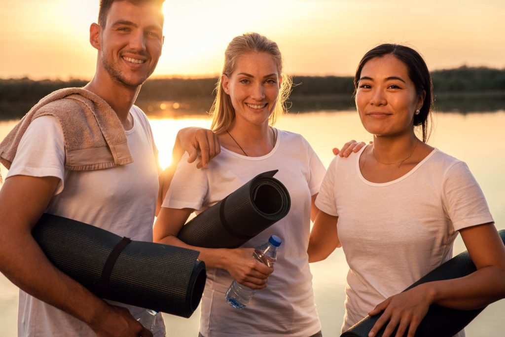 Group of people with yoga mats near the lake looking at camera.